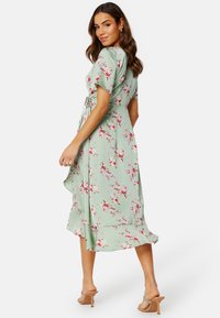 Kwiatowa sukienka w obcisłym kroju z jasnozielonej tkaniny, z różowymi i białymi kwiatami, krótkimi rękawami, wiązaniem w talii i rozkloszowanym dołem.