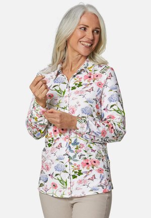 Chemise blanche à boutons avec un motif floral aux accents roses, bleus et verts ; manches longues ; texture de tissu lisse.