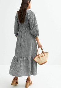 Robe à carreaux noir et blanc avec un ourlet à volants en étages, des manches bouffantes et une taille cintrée ; assortie à un sac à main tissé couleur beige et des sandales à plateforme.