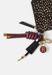 Czarny i brązowy skórzany portfel w kropki z złotymi akcentami, teksturowanymi detalami, bordową brelokiem i medalionem z logo.