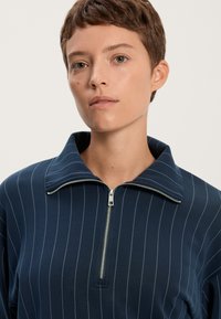 Sötétkék, cipzáros felső, széles gallérral, függőleges világos csíkokkal. Simogatón puha, rugalmas anyagból készült, fém cipzárral.