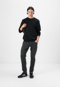 Black sweatshirt with round neckline, gray jeans, and black sneakers featuring white accents. Simple design, casual fit, minimal texture.