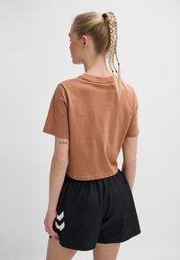Kort brun cropped t-shirt lavet af bomuld, kombineret med sorte shorts med hvide chevron-detaljer. Glat tekstur, afslappet pasform.