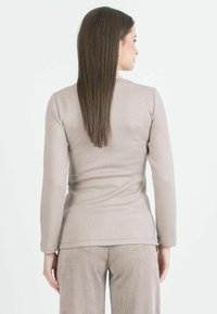 Maglia a maniche lunghe, aderente, in tessuto beige chiaro con una superficie liscia. Presenta un colletto a girocollo e un orlo leggermente curvo in vita.