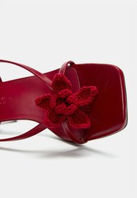 Sandale en cuir rouge à bout carré, ornée d'un accent en fleur en crochet rouge texturé et de fines lanières. Fini lisse sur la semelle.