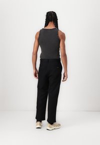 Grå tanktop kombinert med svarte bukser. Stoffet ser glatt ut. Fottøyet er lysfarget med detaljer. Utsikt fra baksiden.