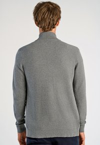 Grå tröja med hög, ribbad krage och texturerad stickad mönster. Har långa ärmar och åtsittande mudd. Vy från baksidan visas.