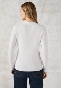 Hellgrauer, gerippter Langarmpullover mit Rundhalsausschnitt, figurbetontem Design und subtiler Textur, kombiniert mit dunkelblauen Jeans mit genähten Taschen.