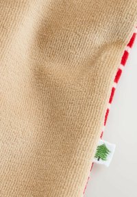Beige tekstuuri kangas, mille ääres on punane ja valge ruuduline muster ning väike valge silt, millel on roheline puu ikoon.