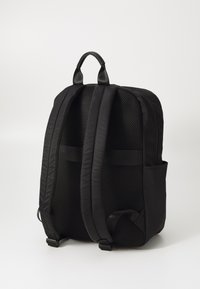 Sac à dos noir avec panneau arrière en maille, bretelles rembourrées et poche latérale. Le tissu lisse et le design moderne mettent en avant la fonctionnalité et le confort.