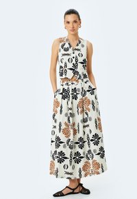Conjunto de dos piezas que incluye una blusa corta y una falda larga. Hecho de tela texturizada con patrones florales en negro y naranja sobre un fondo claro.