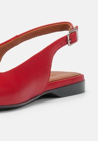 Chaussure rouge en cuir à bride arrière avec un bout arrondi, semelle intérieure beige et un petit talon noir. Dispose d'une boucle ajustable en métal argenté.