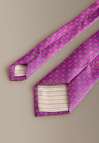 Silk tie featuring a vibrant pink background with a geometric pattern in blue and white, finished with a striped lining. Classic cut design.