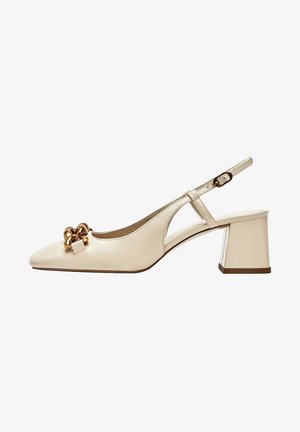 Beżowe skórzane buty na obcasie typu slingback z blokowym obcasem, spiczastym noskiem, regulowanym paskiem i ozdobnym masywnym złotym łańcuchem z przodu.
