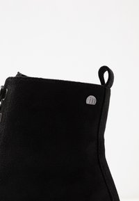 Černá kotníková bota vyrobená z měkkého umělého semiše s hladkým povrchem, obsahující malou logo aplikaci a poutko na patě pro snadnější obouvání.