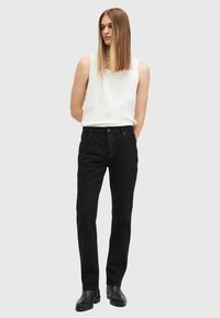 Jeans de mezclilla negra con un corte ajustado, que presentan un clásico diseño de cinco bolsillos y una sutil textura desvaída. Llevados con una camiseta sin mangas blanca ajustada.