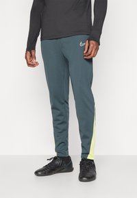 Nike sportovní kalhoty v tmavě modré barvě s žlutými bočními pruhy. Vyrobené z pružného materiálu, s těsným střihem a elastickým pasem.