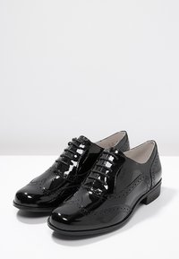 Chaussures Oxford en cuir verni noir avec un design à bouts fleuris, bout rond et fermeture à lacets. Caractérisées par des perforations décoratives et un petit talon.
