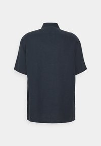 Chemise bleu marine foncé à manches courtes avec un empiècement dans le dos et un col classique, vue de dos sur un fond clair uni.