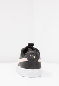 Baskets en cuir noir avec une bande rose, logo doré et semelle en caoutchouc blanc texturé. Comprend une languette pour un enfilage facile.