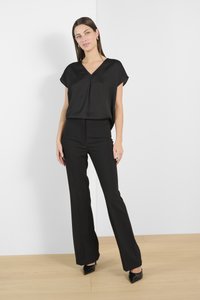 Sort kortærmet bluse med V-udskæring, parret med tætsiddende sorte bukser. Begge har en glat tekstur, skræddersyet design og minimale detaljer.