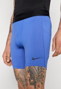 Blå idrettsshorts i stretchy stoff, med en svart elastisk linning merket "NIKE PRO" og en liten svart swoosh-logo på siden.
