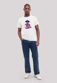 White t-shirt featuring a colorful graphic of a person in a hat, paired with blue jeans and white sneakers. Simple, casual design.