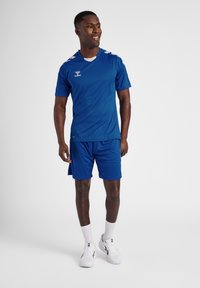 Blå sportstrøje og shorts sæt lavet af letvægtsstof, med rund hals, korte ærmer, og hvide detaljer på skuldrene.