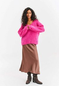 Ružový huňatý sveter s výstrihom do V a širokými rukávmi, skombinovaný s hnedou saténovou sukňou a hnedými členkovými čižmami so striebornými akcentmi.