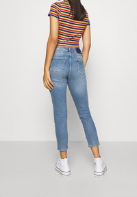 Höga blå denimjeans med ljus tvätt, avsmalnande ben och två bakfickor, i kombination med en flerfärgad randig t-shirt och vita sneakers.