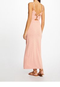 Robe maxi en rose clair, dotée d'un motif en zigzag et d'une découpe au dos avec une boucle. Design à bretelles, confectionnée en tissu tricoté texturé.