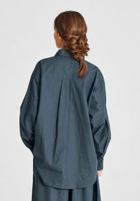 Dunkelgraues Langarmshirt mit einem lässigen Schnitt, umklappbarem Kragen und Rückenfalten-Detail, hergestellt aus einem leichten, strukturierten Stoff.