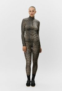 Conjunto atlético de estampado de leopardo en tejido elástico; camiseta de manga larga con media cremallera, leggings ajustados, acompañados de zapatillas deportivas negras.