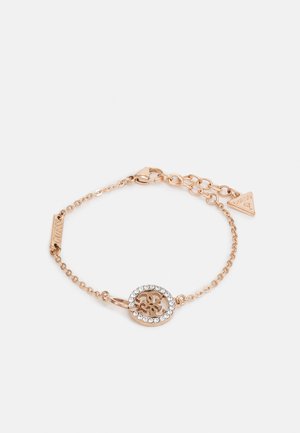 Bracelet chaîne en or rose avec un pendentif circulaire présentant un motif découpé entouré de petits cristaux clairs et un fermoir ajustable avec une étiquette logo.