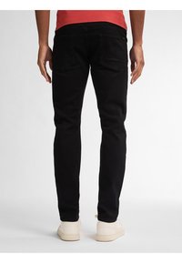 Zwarte denim jeans met een slim fit, voorzien van twee achterzakken en een gladde textuur. Gedragen met witte sneakers en een rood shirt.