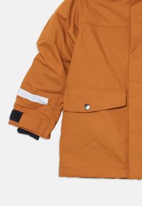 La manche de la veste imperméable orange présente une bande réfléchissante blanche et une poche à bouton-pression, avec une finition texturée et un poignet noir.