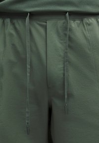 Pantaloni sportivi grigio-verdi con superficie strutturata, cintura elastica e lacci con punte in plastica.