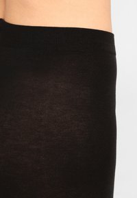 Schwarze Leggings aus weichem, dehnbarem Stoff. Der Bund ist breit und elastisch, was eine enge Passform mit einer glatten Textur gewährleistet.