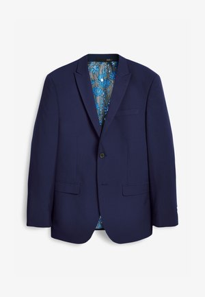 Marineblauer Anzug mit figurbetontem Schnitt, kombiniert mit einem hellrosa Hemd mit gemustertem Kragen. Braune Lederschuhe runden das Outfit ab.