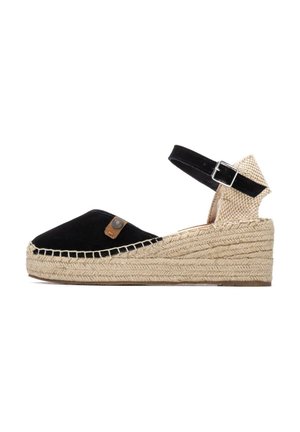 Cuña de esparto de ante negro con suela de cuerda de yute, correa en el tobillo y detalles tejidos. Cuenta con una pequeña etiqueta de marca en el lateral.