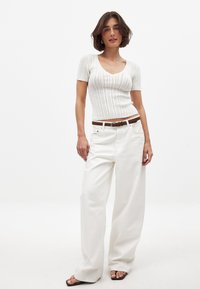 Hvid strikket kortærmet top med ribbet tekstur, parret med højtaljede hvide brede jeans og et brunt læderbælte.
