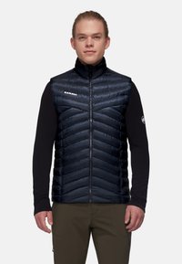 Mit Wattierung, ärmellose Weste in Dunkelblau mit hohem Kragen, mit Zickzack-Nähten und einem Logo auf der linken Seite. Leichter Stoff.