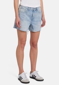 Shorts in denim azzurro chiaro con orlo sfrangiato, design a cinque tasche e vestibilità rilassata. Abbinati a sneaker grigie e bianche con strisce nere.