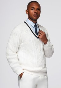Maglione bianco spesso a maglia con scollatura a V e motivo testurizzato, con bordo blu navy scuro. Indossato sopra una camicia colletto azzurro e una cravatta.