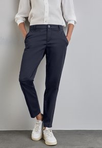 Navy broek met een slim fit, gemaakt van lichtgewicht stof. Voorzien van twee zijzakken en een knoopsluiting. Gecombineerd met witte sneakers.