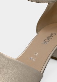 Μπεζ δερμάτινο σανδάλι με λεία υφή, πλατιά λωρίδα πάνω από το πόδι και χαμηλό χοντρό τακούνι. Διαθέτει λογότυπο της μάρκας στην εσωτερική σόλα και ενδείξεις μεγέθους.