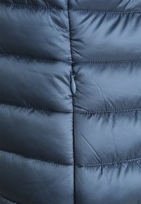 Marineblaue Pufferweste mit gesteppter Optik, die genähte Abschnitte und einen kleinen Reißverschlusszug hat. Glatte, leichte Stofftextur.