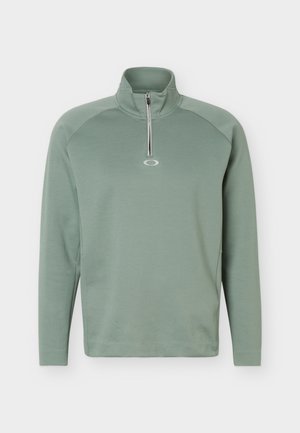 Polo à manches longues vert clair avec une courte fermeture éclair au niveau du col et un petit logo centré sous la fermeture éclair.