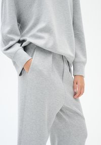 Grijze sweatshirt en bijpassende broek van zacht materiaal, met een ontspannen pasvorm, verlaagde schouders en zijzakken voor comfort.