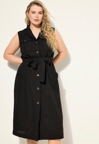 Vestito nero senza maniche con bottoni frontali, due tasche sul petto, vita claudicante e orlo a ginocchio. Realizzato in tessuto leggero.